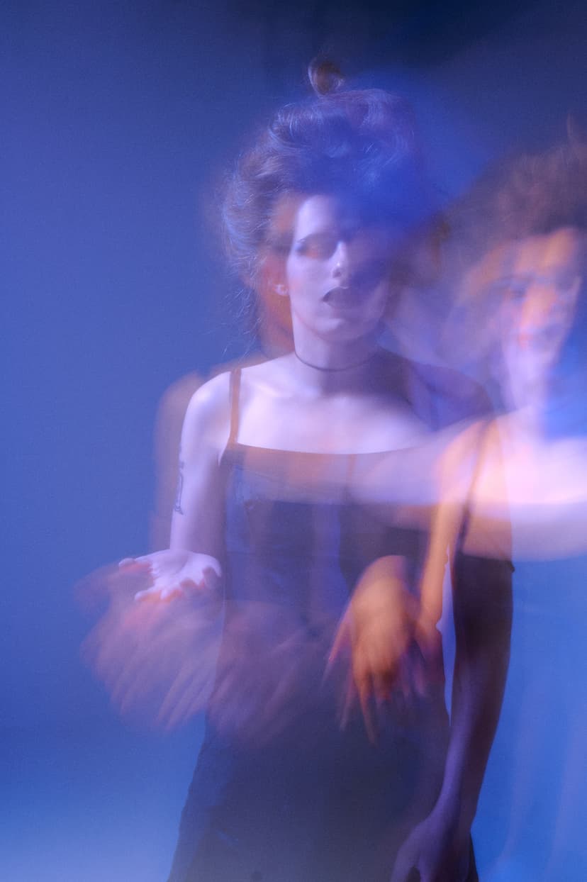 A woman on a black dress in purple lighting, with a shade of herself in orange color, creating a sense of being an enchantress